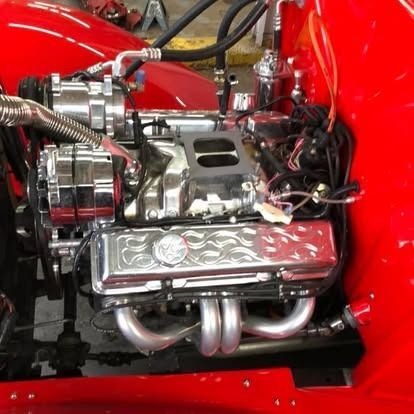 A red car has a chrome engine with flames on it