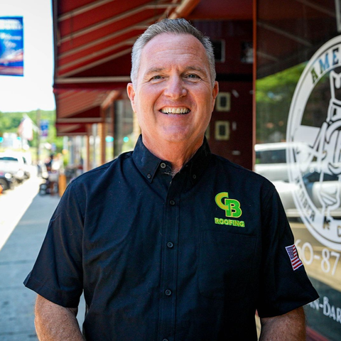 Smiling man in a black shirt standing outside a storefront under a red awning