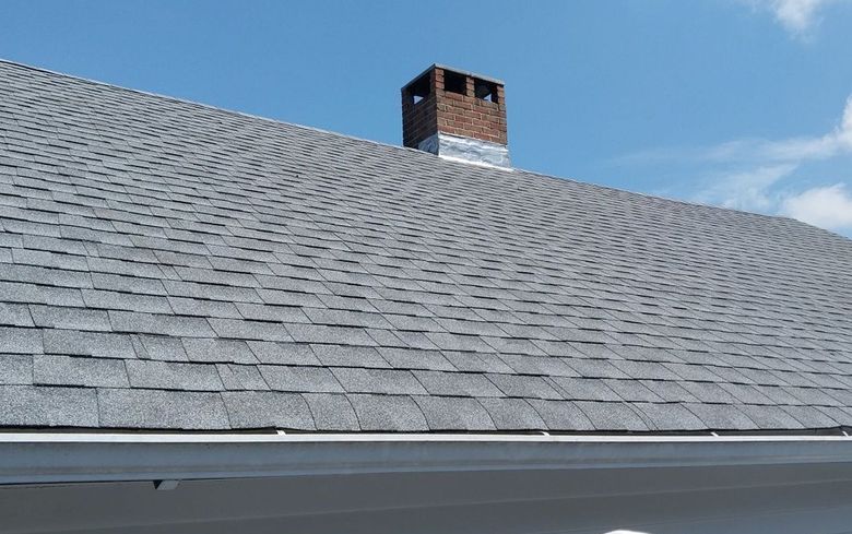 Gray shingled roof with a brick chimney against a blue sky