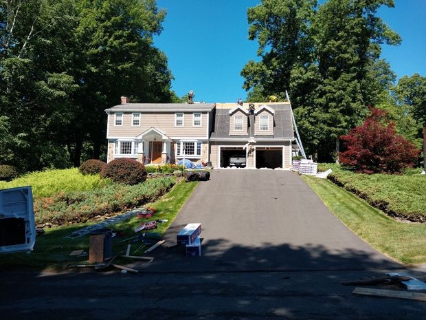 Suburban house with a long driveway, garage, and green trees on a sunny day