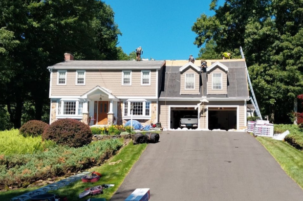 Suburban house with a long driveway, garage, and green trees on a sunny day
