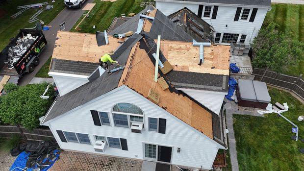 Aerial view of a house roof under repair with workers, exposed plywood, and debris around the property