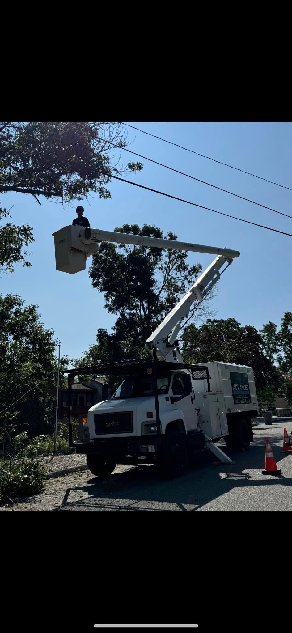 Utility truck with raised bucket lift working near overhead power lines on a sunny street