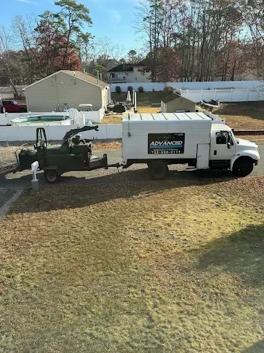 White utility truck with lift equipment parked on grass in a suburban yard, trees and houses in background