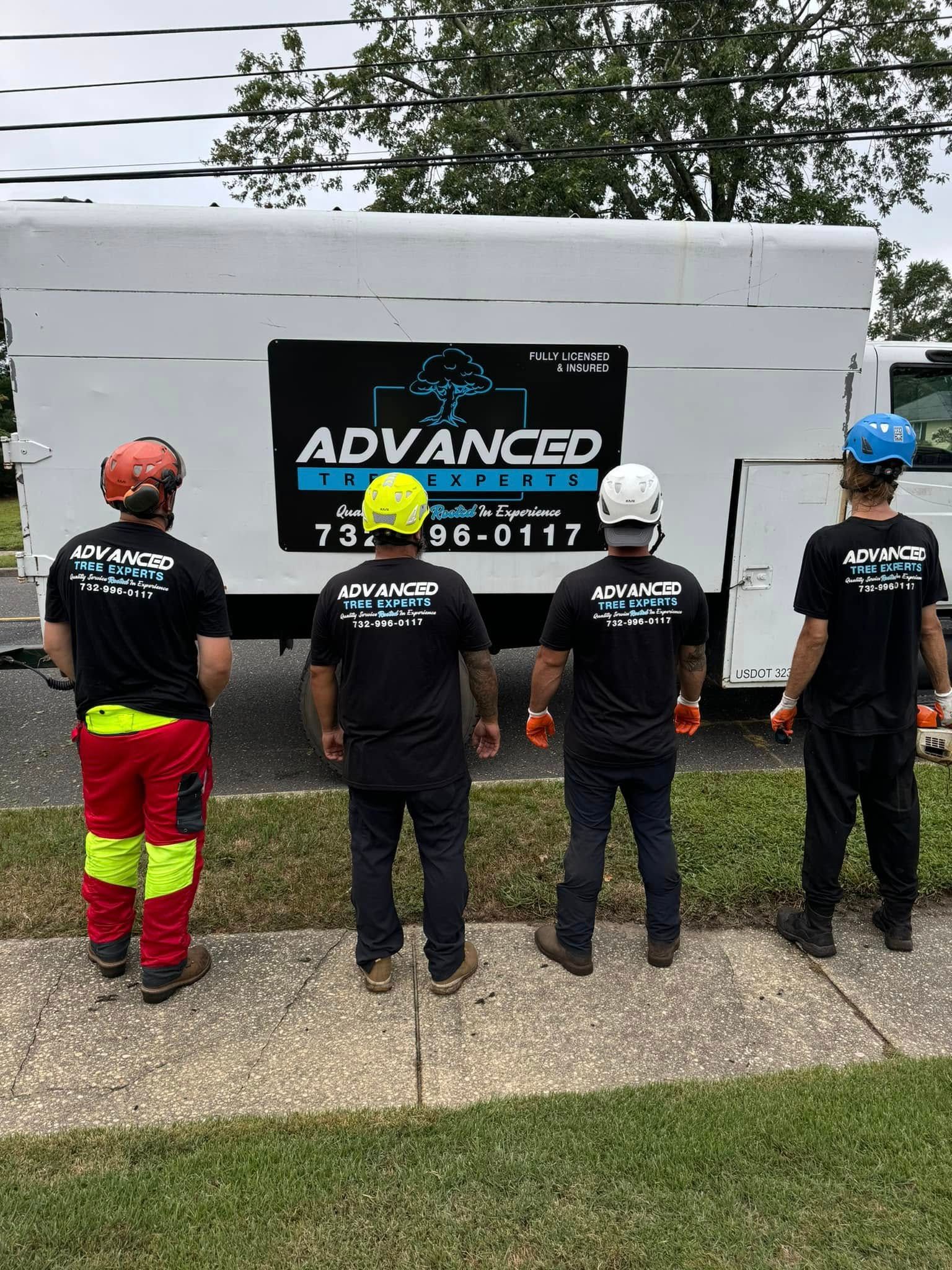 Four utility workers in hard hats inspect a white utility trailer with an ADVANCED sign outdoors.