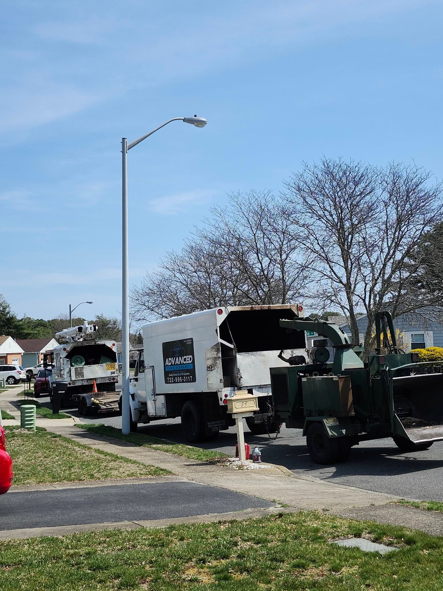 Street scene with utility trucks and a crane parked near houses under a blue sky