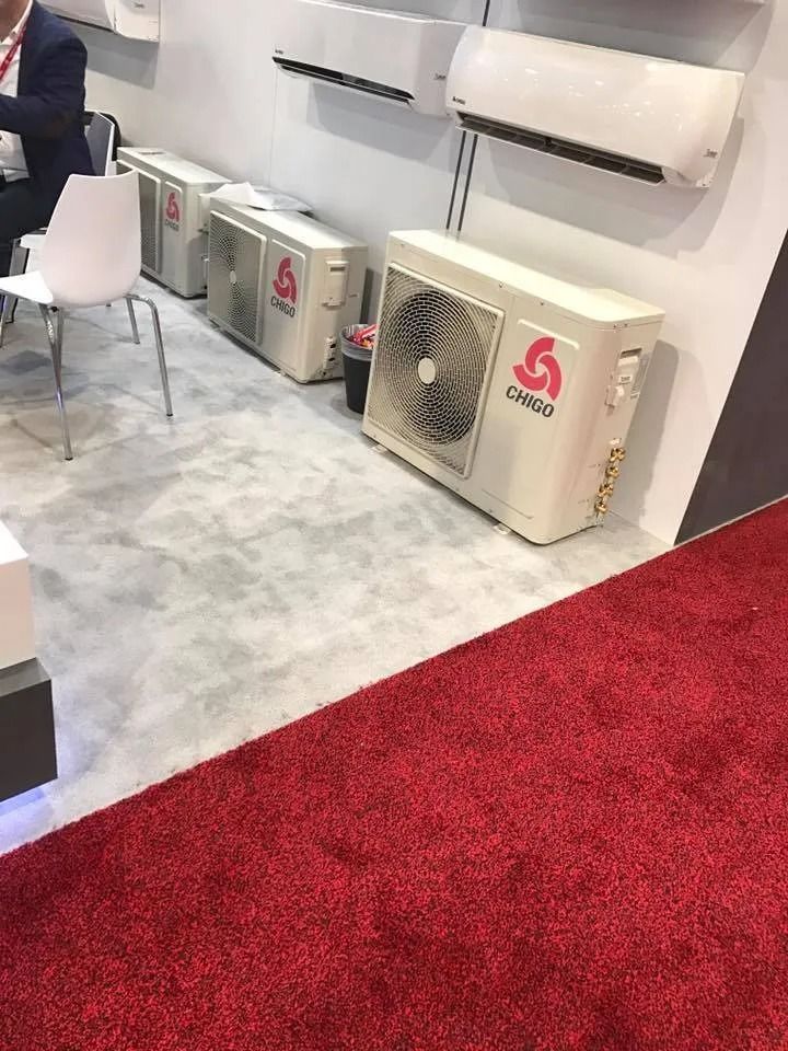 Trade show booth with HVAC outdoor units and wall-mounted air conditioners on a gray floor, red carpet edge in front