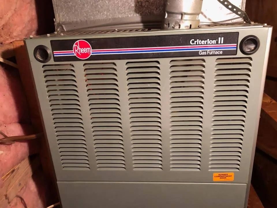 Rheem Criterion II furnace in a basement, with gray front vents and brick wall behind it