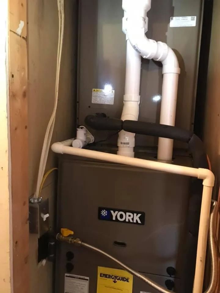 York furnace and white PVC pipes in a utility closet with a black insulated line and yellow tag
