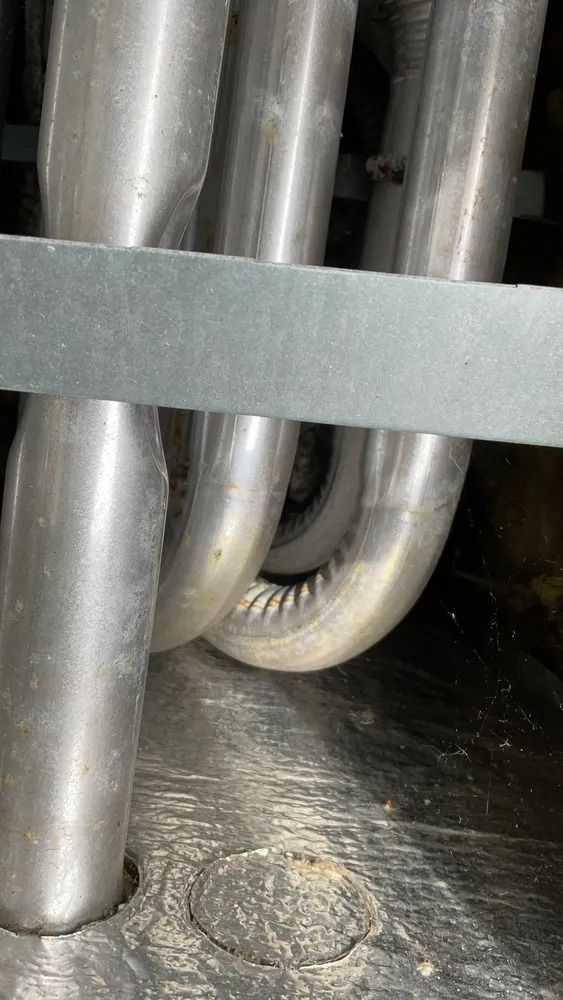 Close-up of shiny metal pipes behind a gray strap in a dim industrial setting