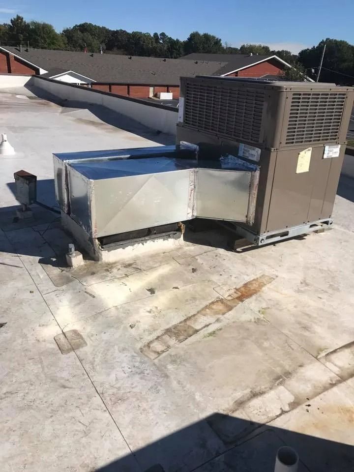 Rooftop HVAC unit with metal ductwork on a flat white roof under clear sunlight.