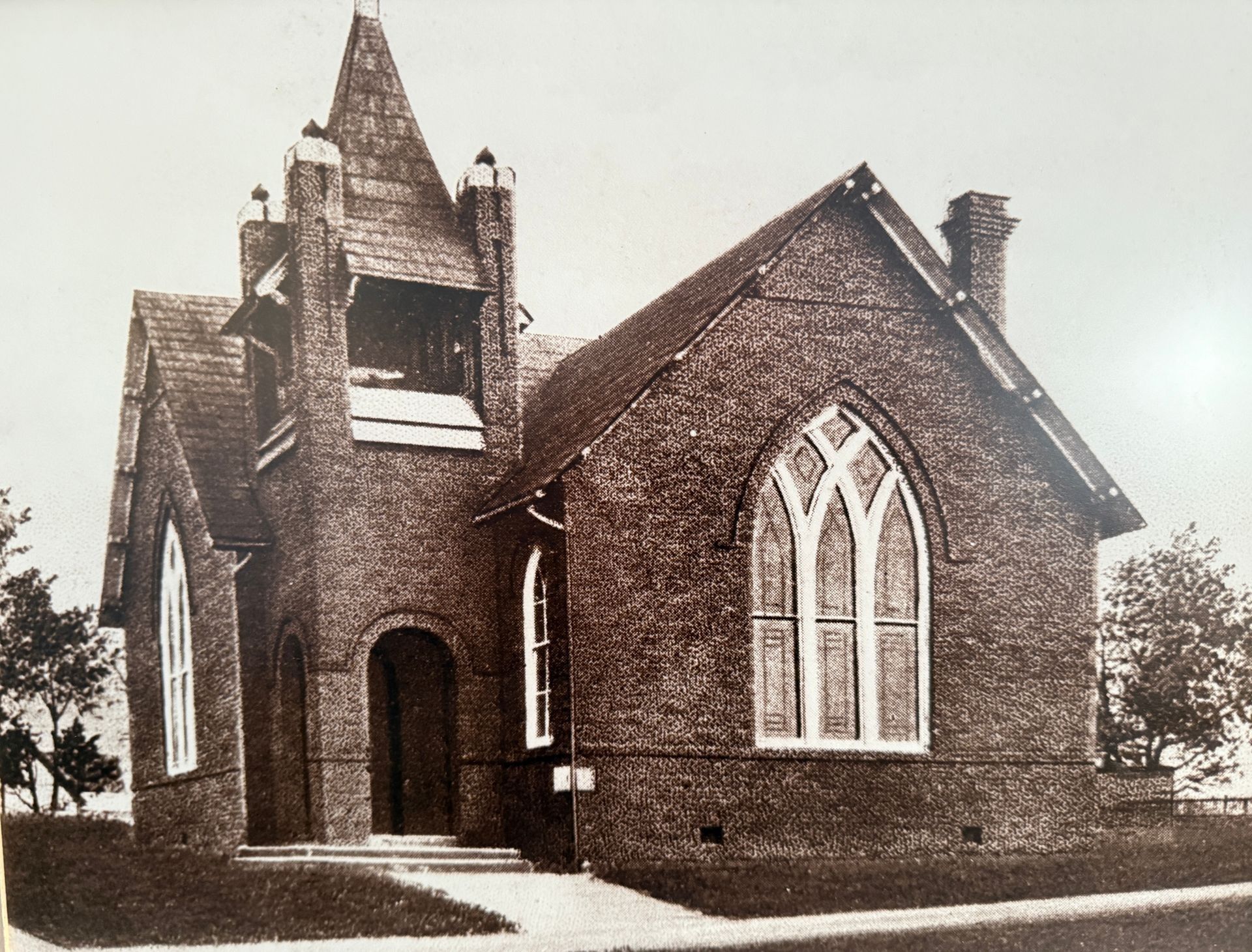 Old brick church with pointed tower, arched windows, and a small entrance path.