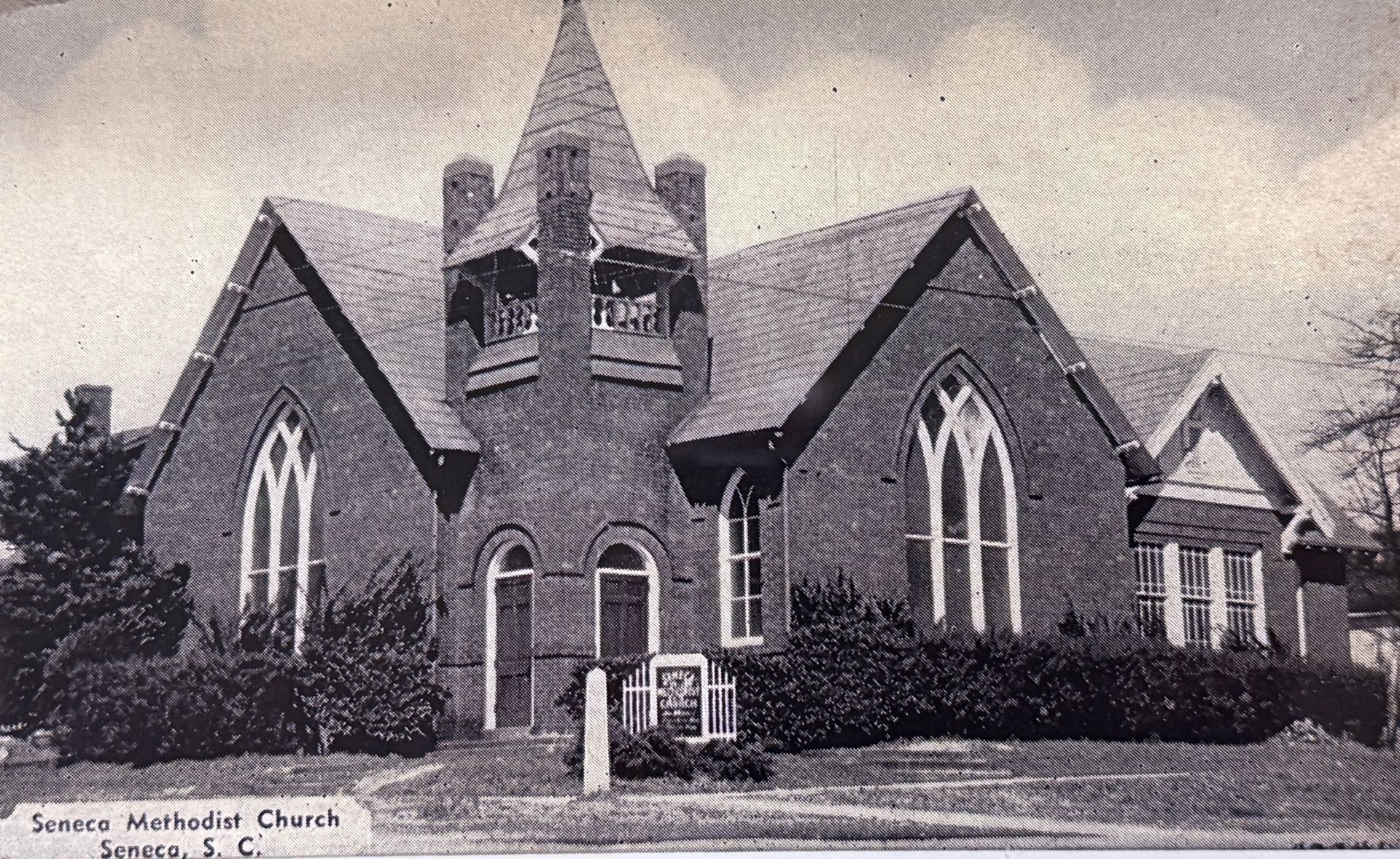 Old brick church with a central steeple and arched windows, seen from the front on a cloudy day