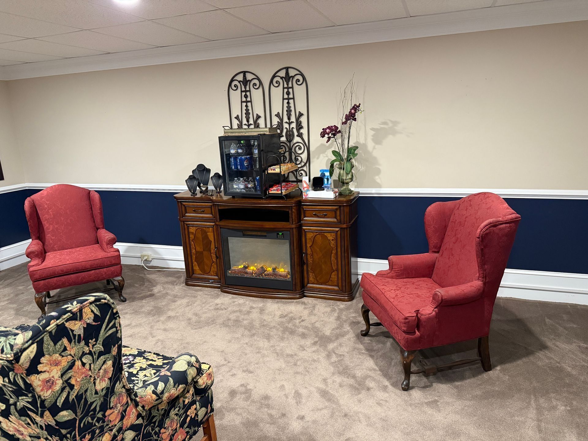 Quiet lounge with red armchairs, ornate wooden console, floral arrangement, and patterned sofa against a blue wall.
