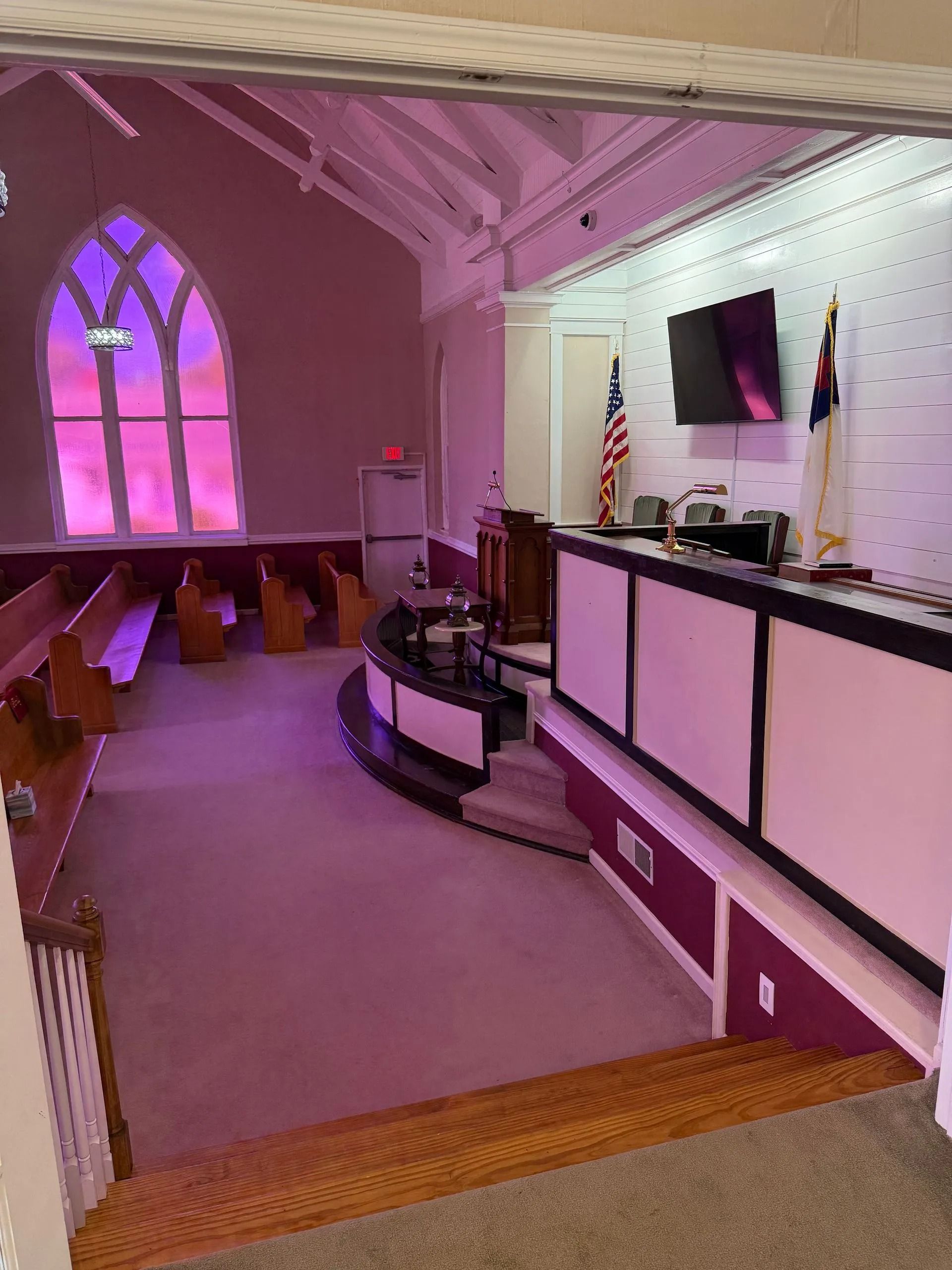 Church interior with pews, stained-glass window, and a raised stage with flags and a screen