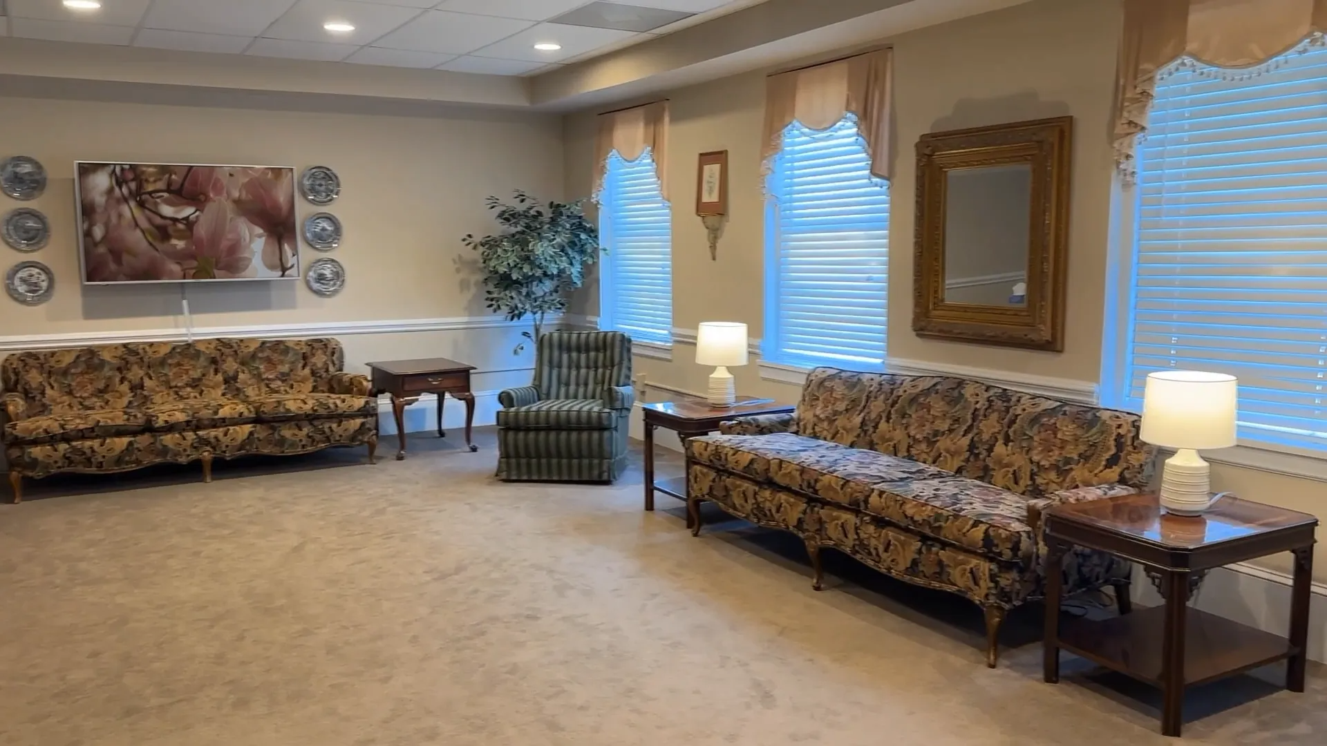 Empty waiting room with patterned sofas, lamps, framed art, and beige carpet.