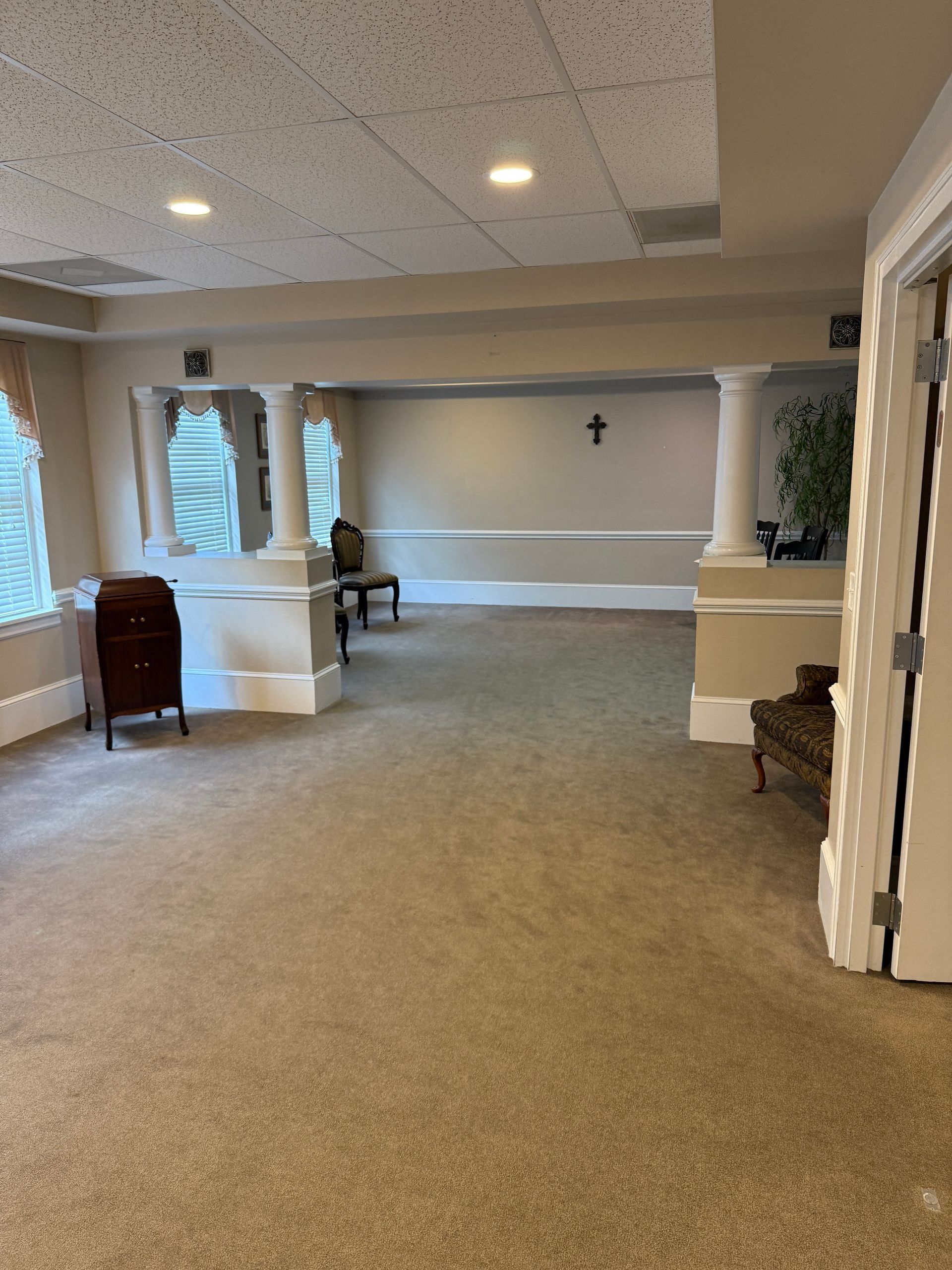 Spacious beige lobby with carpet, columns, windows, bench, and wall cross.