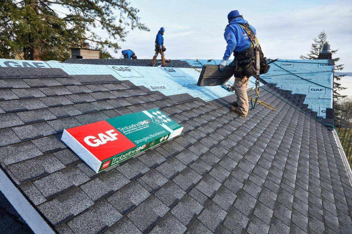 A man is standing on top of a roof with a bag of shingles on it.