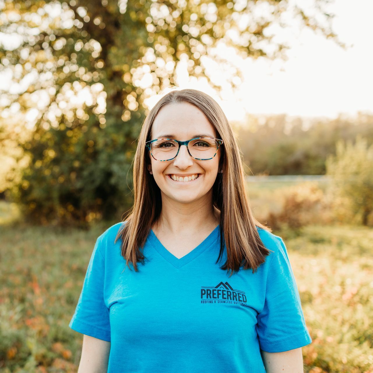 A woman wearing glasses and a blue shirt is standing in a field.