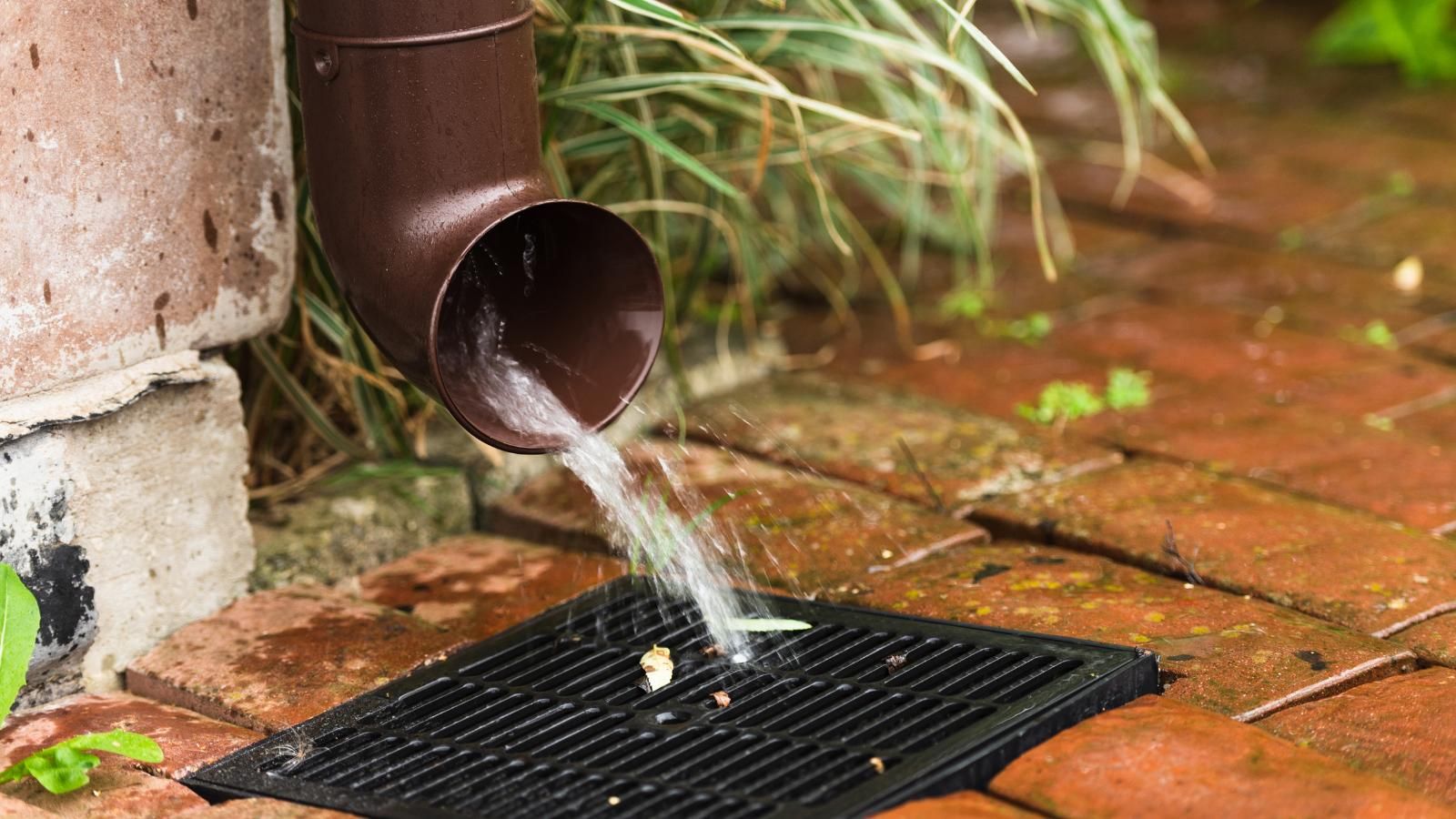 gutter and french drain Brown gutter draining water onto a black grate set in brick.