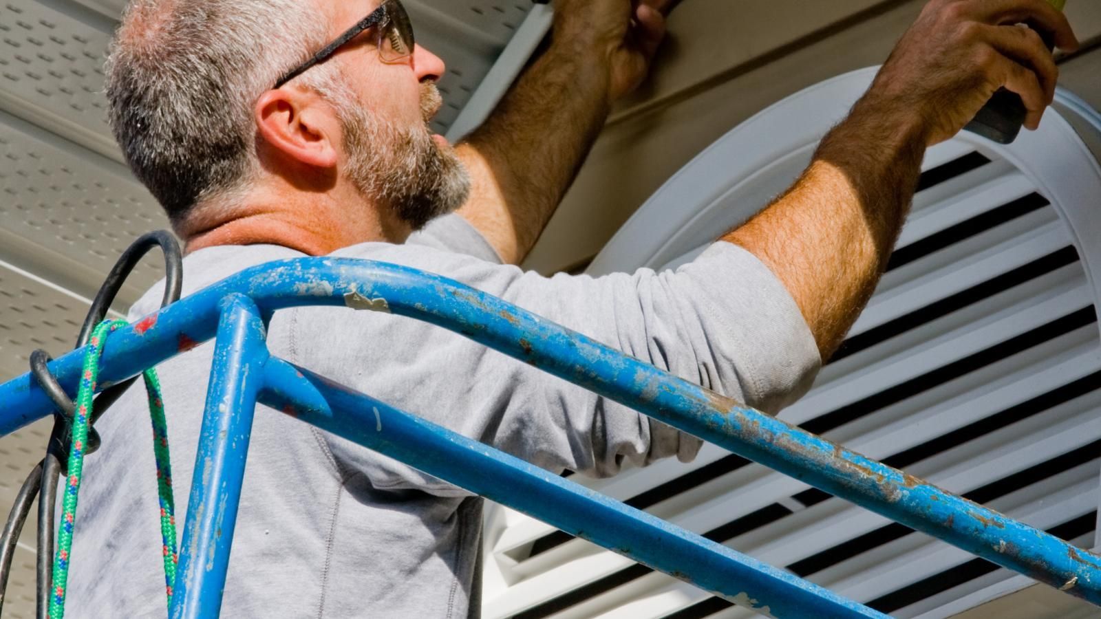 replacing house siding A man is standing on a ladder working on a vent.