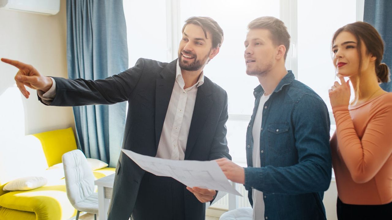 A man is pointing at something while a woman looks on while a man holds a piece of paper.