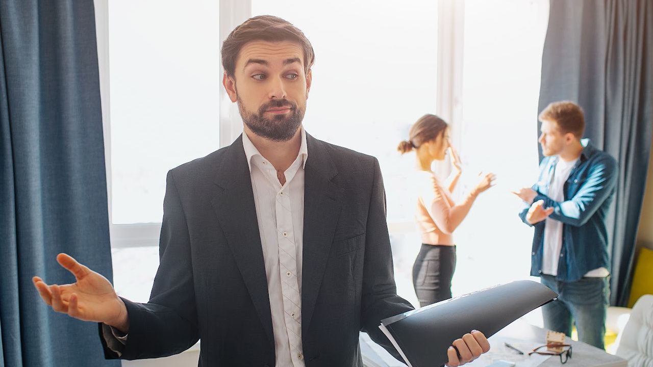 A man in a suit is standing in front of a woman in a hotel room.