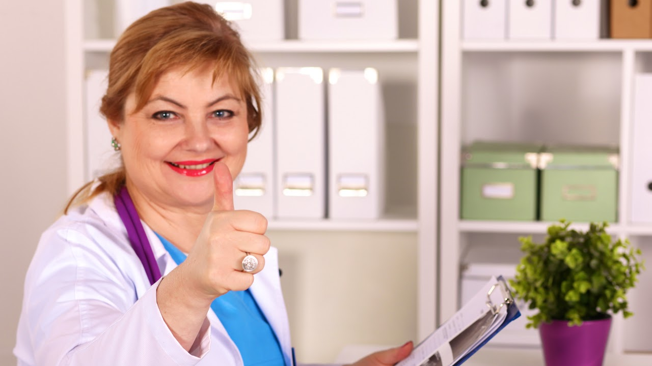 A female doctor is giving a thumbs up sign while holding a clipboard.