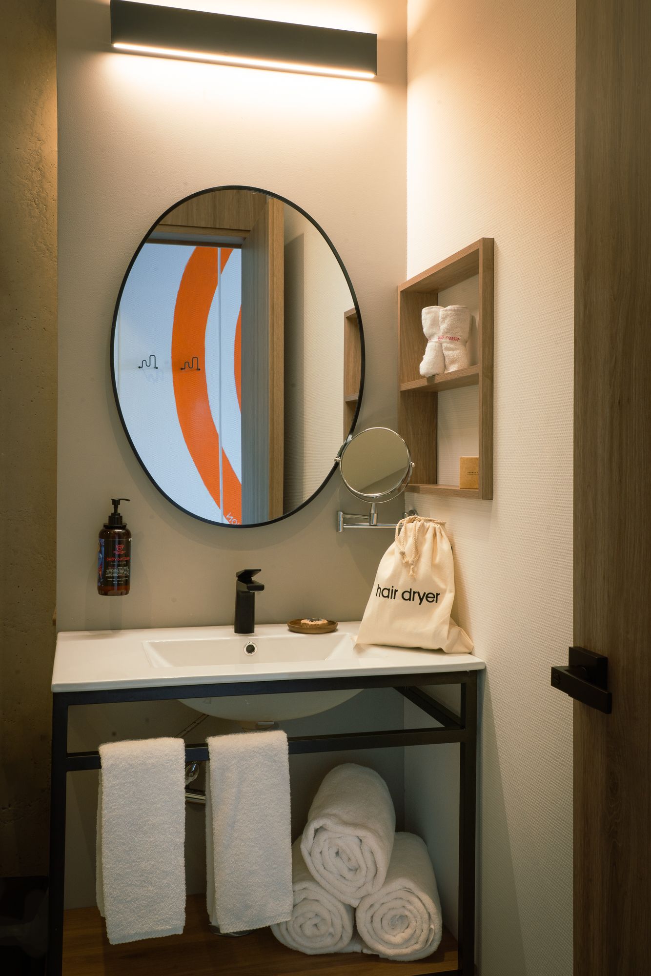 Bathroom with round mirror, sink, and towels. Includes a shelf with towels and hairdryer.