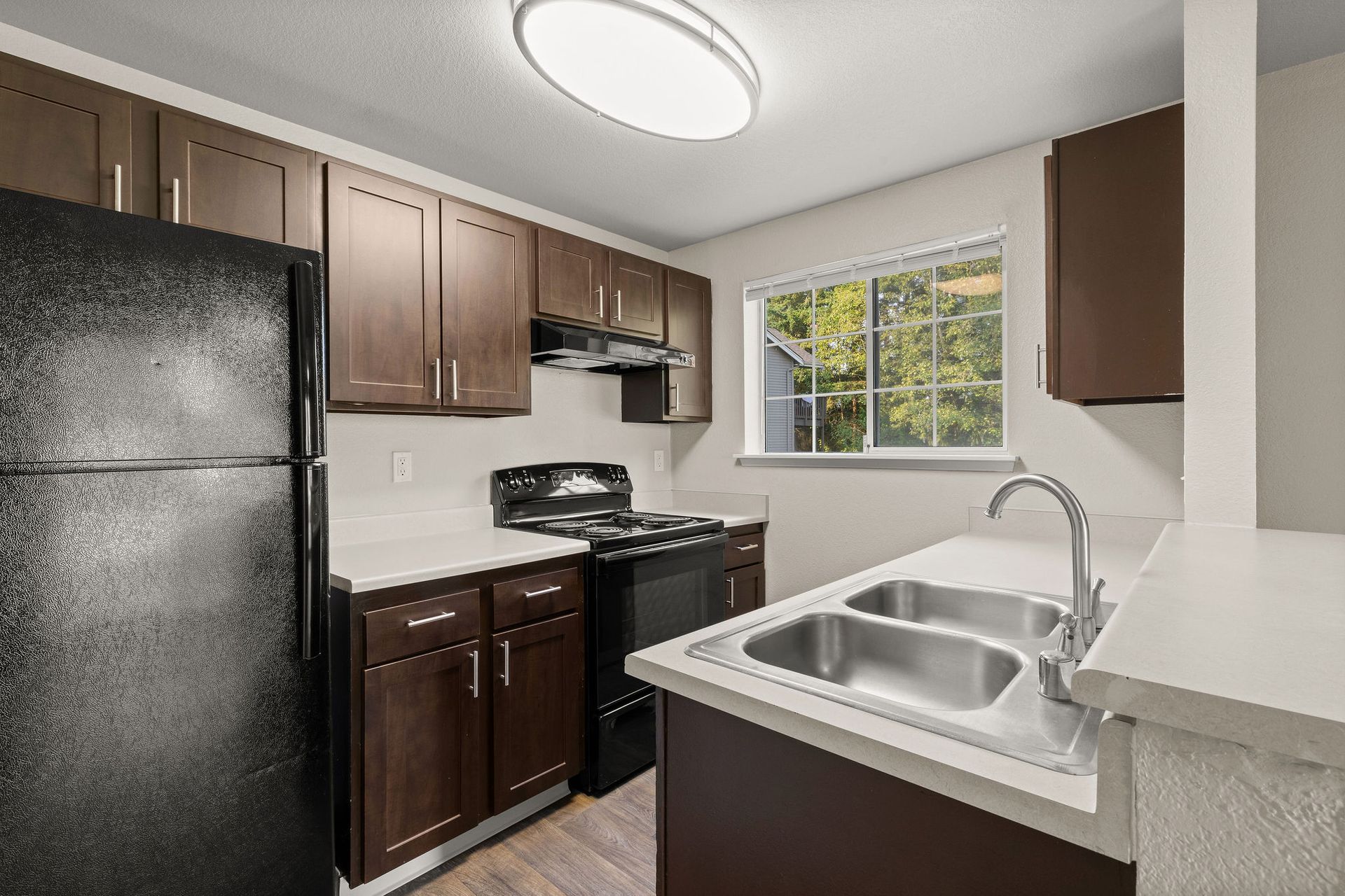 Kitchen with dark brown cabinets, black appliances, light countertops, and a window.