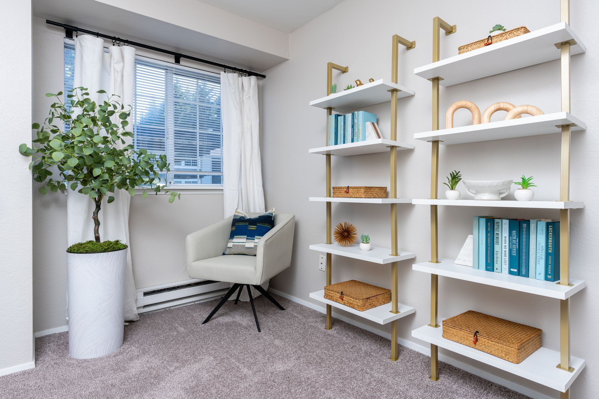 Cozy reading nook with a chair, bookshelf, potted plant, and window with curtains.