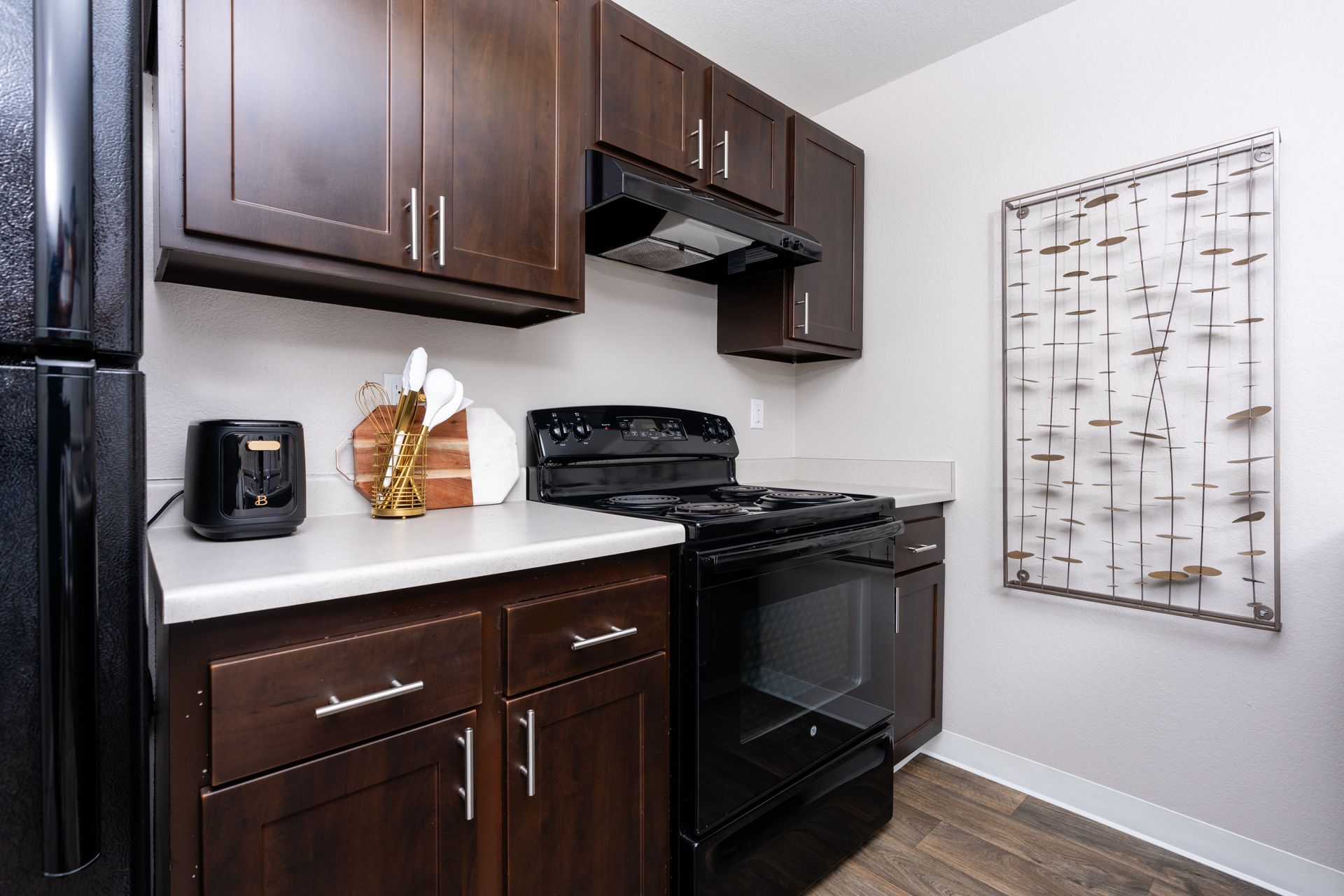 Kitchen with black appliances, dark brown cabinets, white countertop, and wall decor.