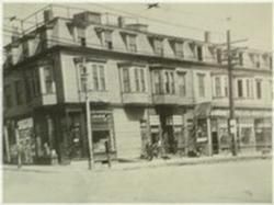 Sepia-toned street scene with a row of old storefront buildings and pedestrians on the sidewalk