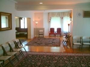 Empty living room with chairs, rugs, and a windowed sitting area with a lamp.