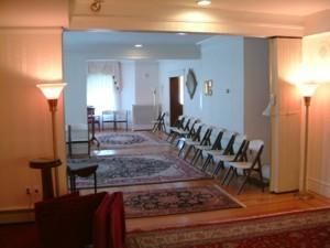 Long banquet hall with patterned rugs and rows of folding chairs along the right wall