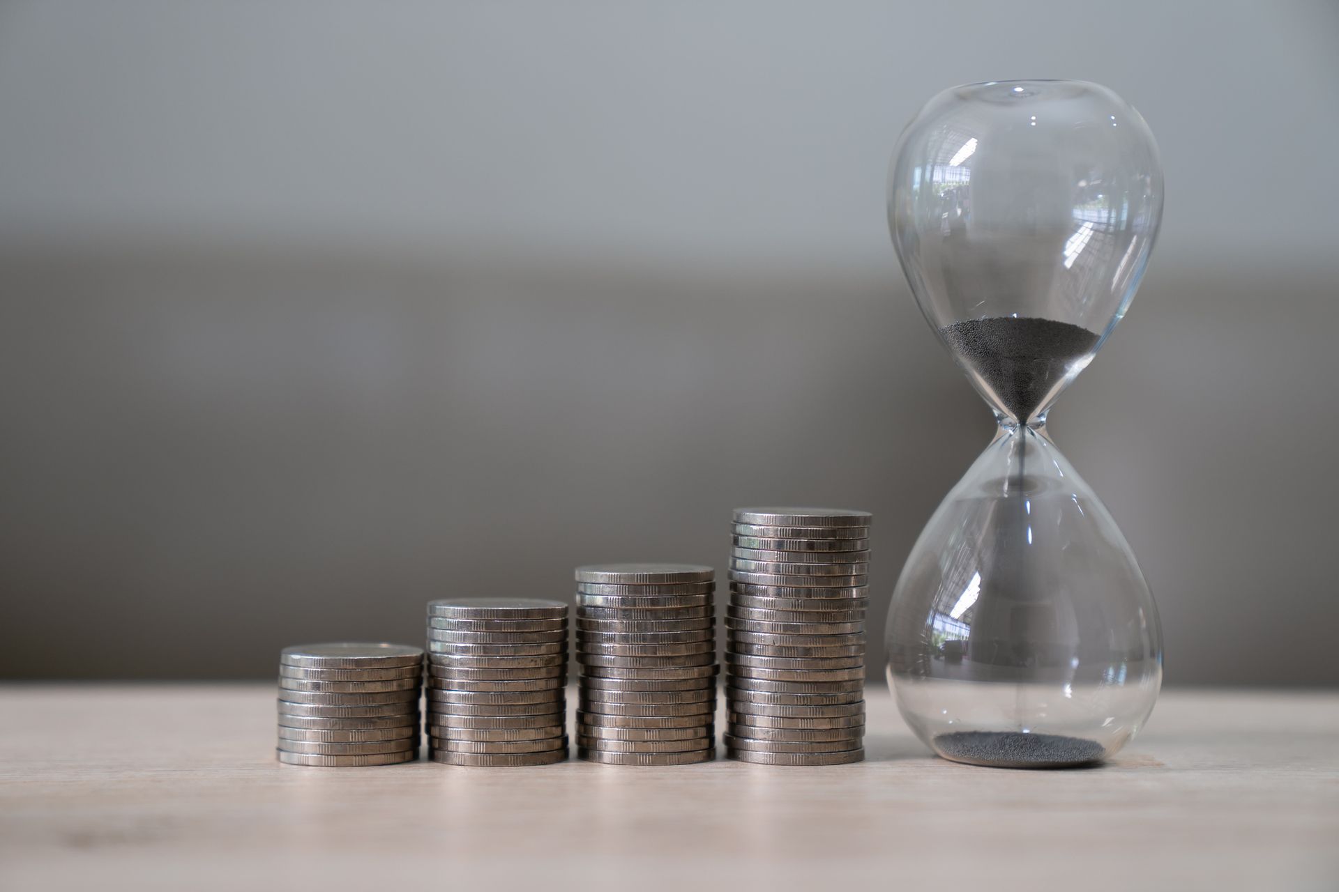 A hourglass is sitting next to stacks of coins on a table.
