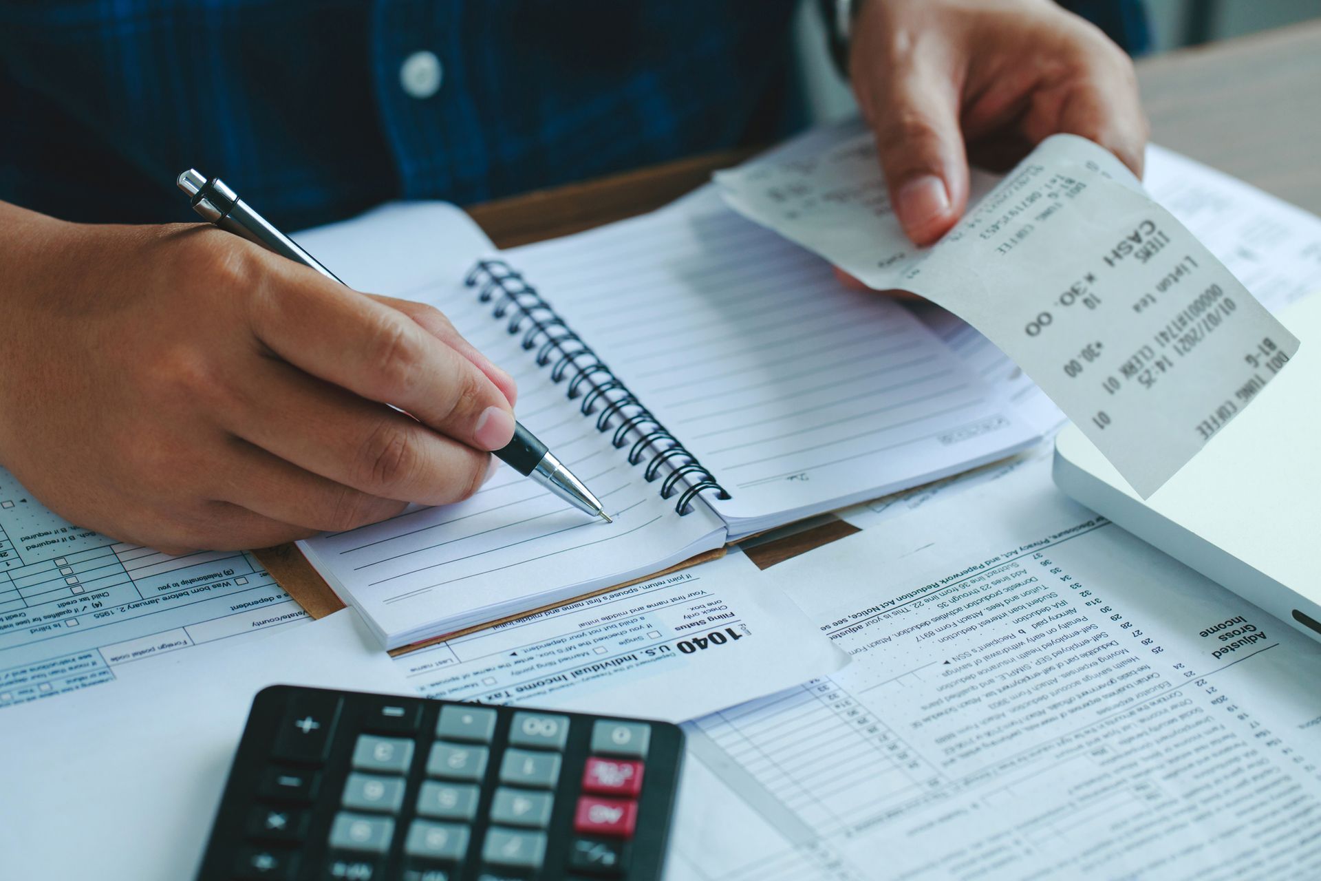 A person is sitting at a table holding a receipt and writing in a notebook.