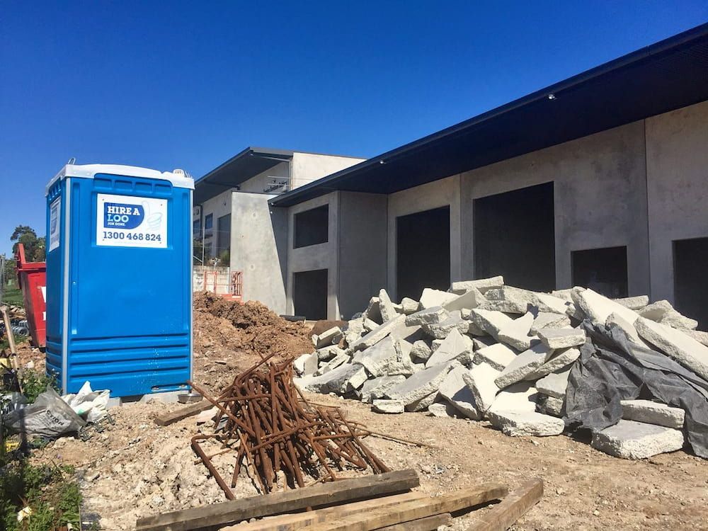 A Blue Portable Toilet in Front of a Building Under Construction — Hire A Loo in Caloundra, QLD