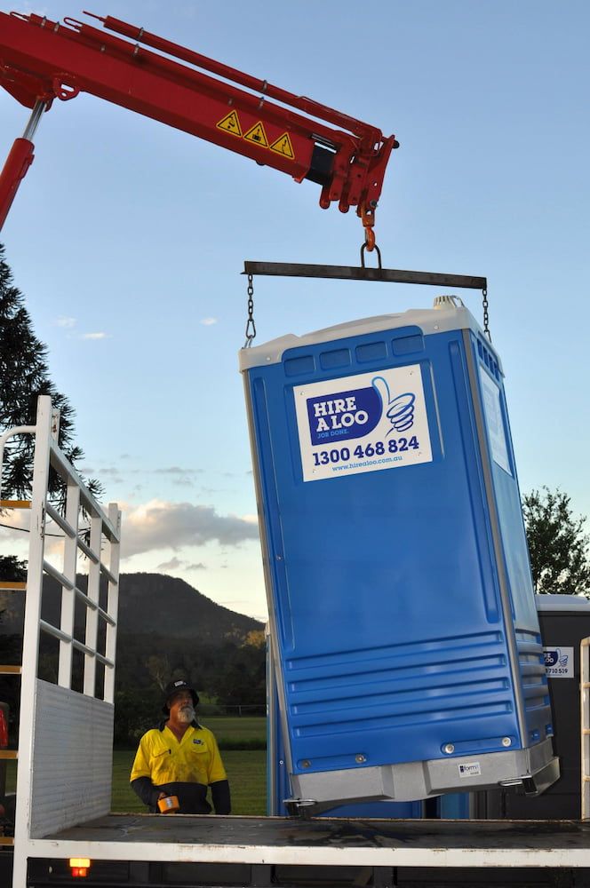 A Blue and White Portable Toilet is Being Lifted by a Crane — Hire A Loo in Coolum Beach, QLD