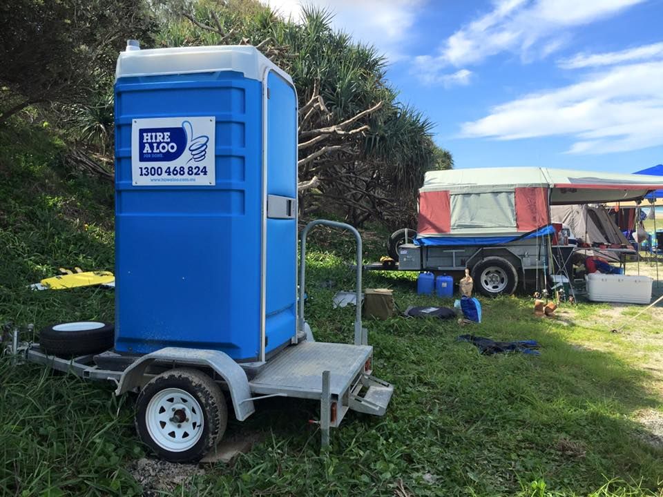 A Blue Portable Toilet is on a Trailer in a Grassy Field — Hire A Loo in Coolum Beach, QLD