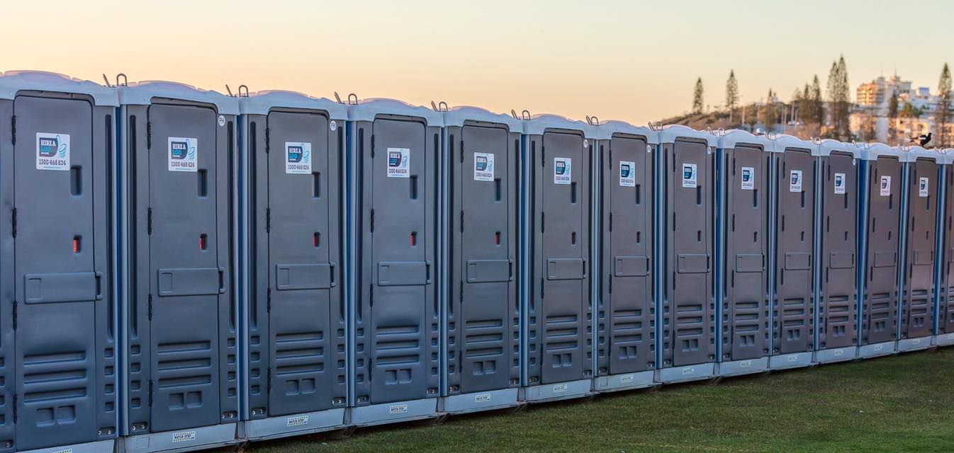 A Row of Portable Toilets Are Lined Up in a Field — Hire A Loo in Noosa, QLD