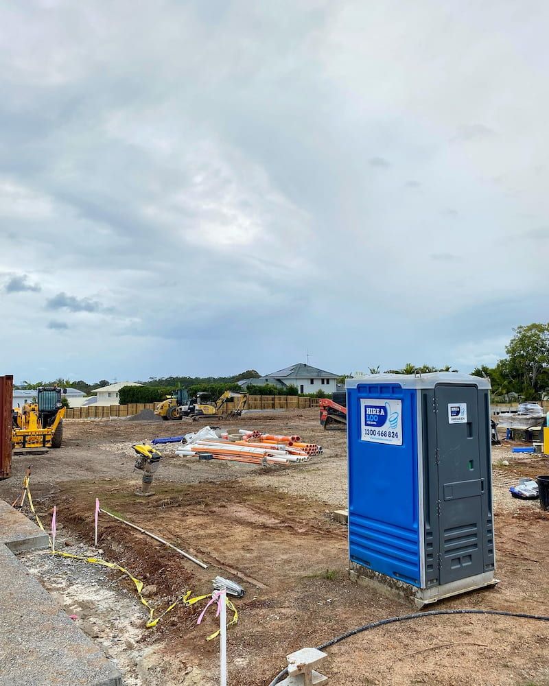 A Blue Portable Toilet is Sitting in the Middle of a Construction Site — Hire A Loo in Mooloolaba, QLD