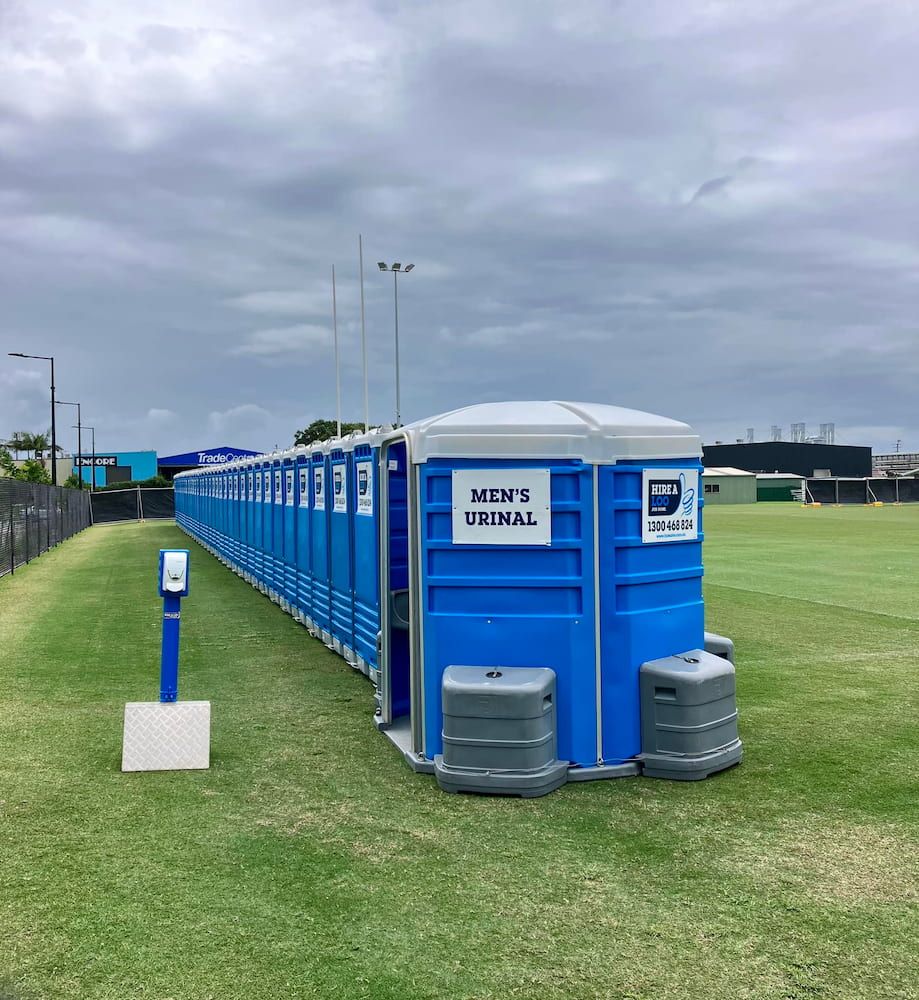 A Row of Blue Portable Toilets Are Lined Up in a Grassy Field — Hire A Loo in Coolum Beach, QLD