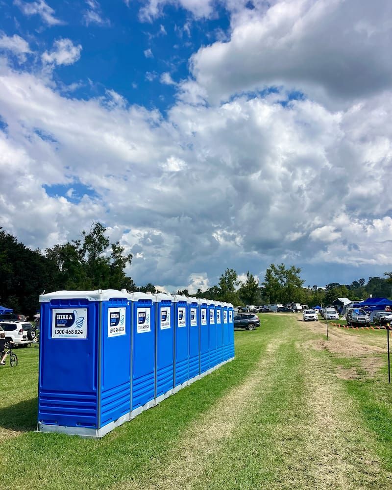 A Row of Blue Portable Toilets Are Lined Up in a Grassy Field — Hire A Loo in Mooloolaba, QLD