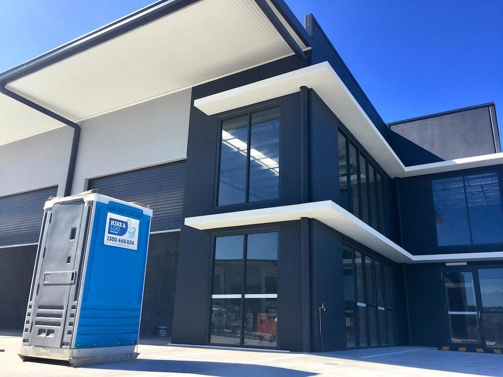 A Blue Portable Toilet is Parked in Front of a Large Building — Hire A Loo in Caloundra, QLD