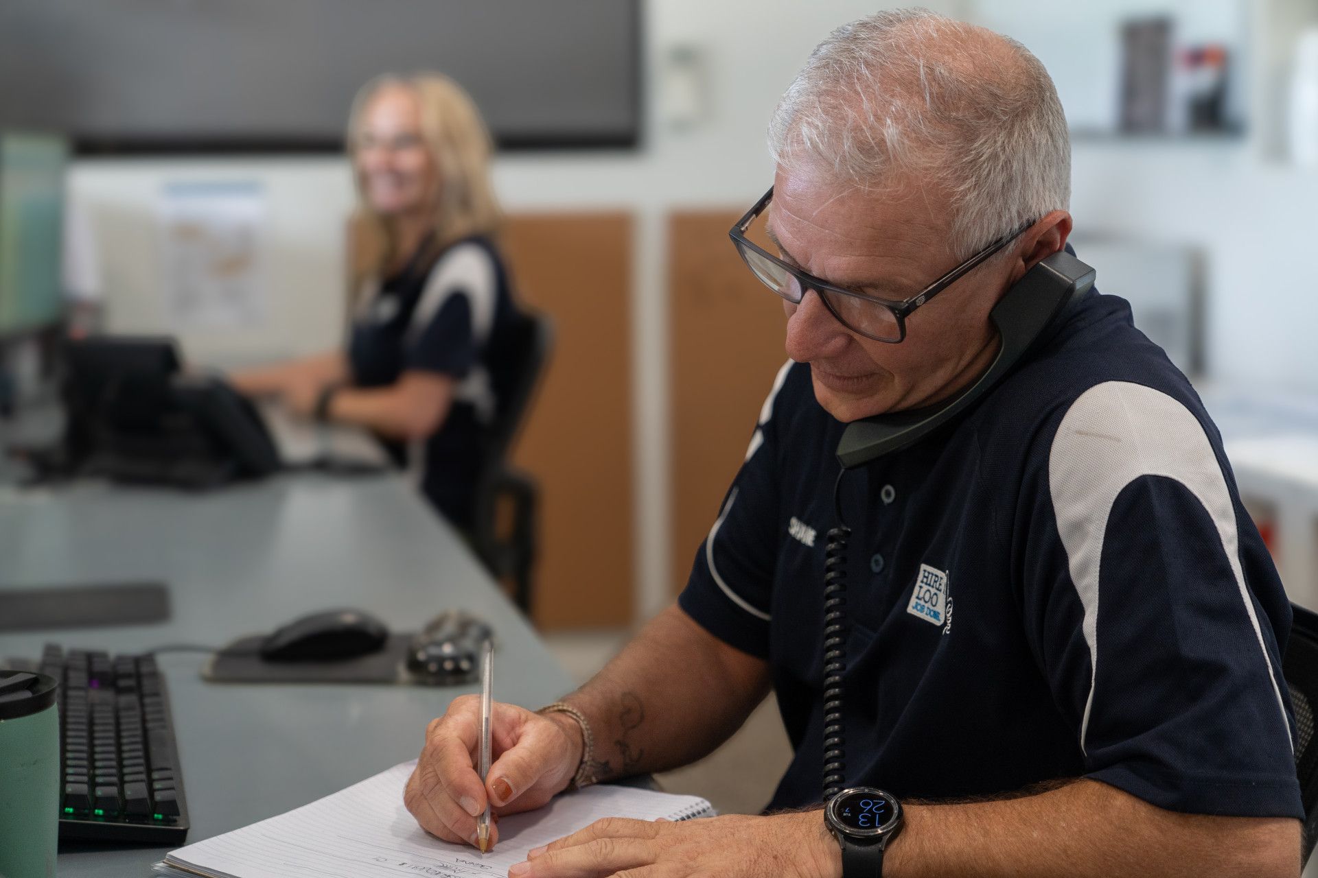 Man On Phone Call With Lady At Desk In Background — Hire A Loo in Coolum Beach, QLD
