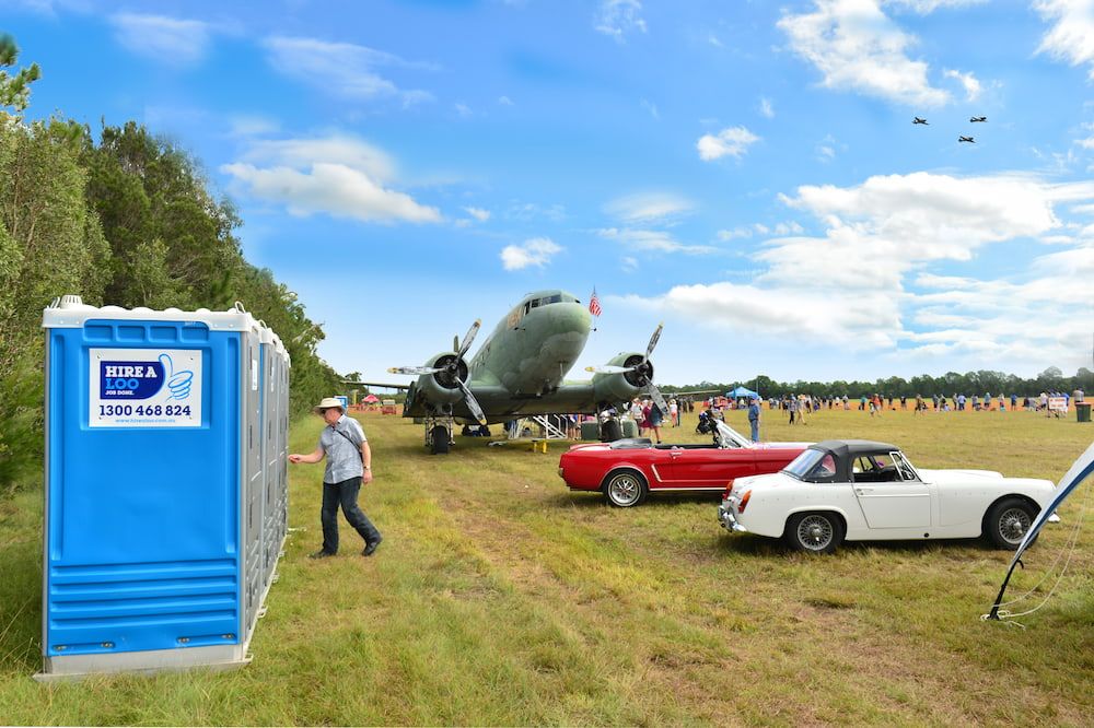 A Man is Standing Next to a Blue Portable Toilet in a Field — Hire A Loo in Nambour, QLD