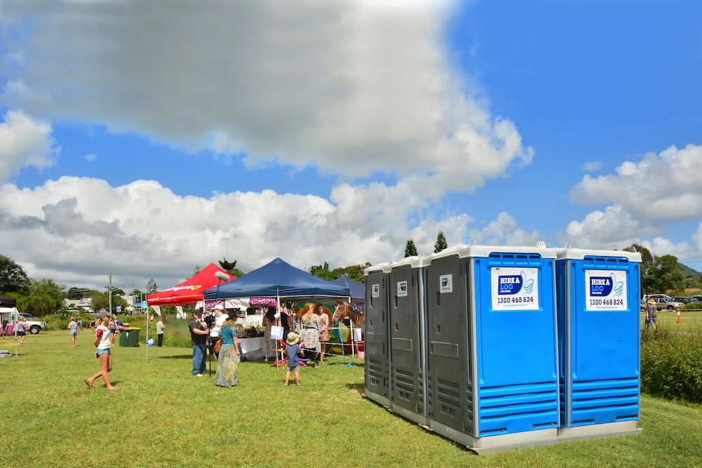 Two Blue Portable Toilets Are Sitting in a Grassy Field — Hire A Loo in Caloundra, QLD