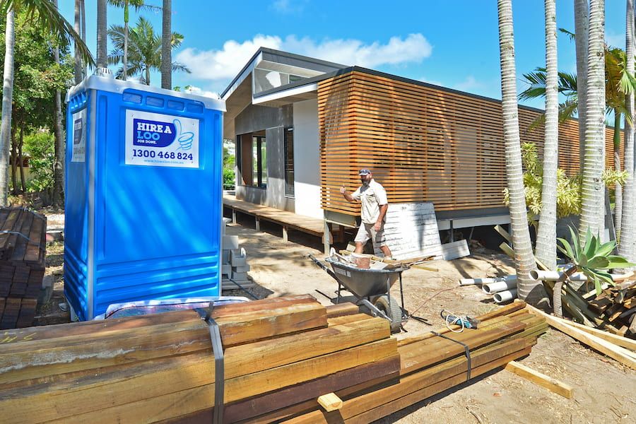 A Blue Portable Toilet is Sitting Next to a Pile of Wood — Hire A Loo in Coolum Beach, QLD