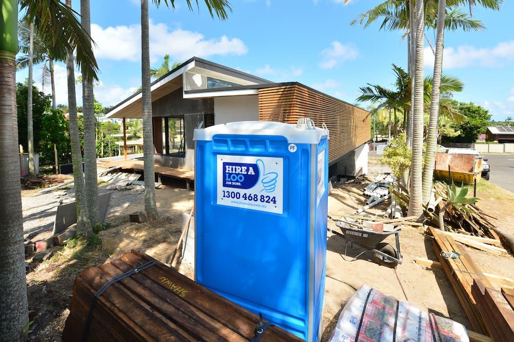A Blue Portable Toilet is Sitting in Front of a House — Hire A Loo in Mooloolaba, QLD